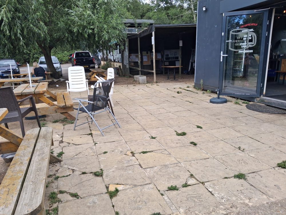 The dark timber café cabin with picnic benches on the paved terrace under trees